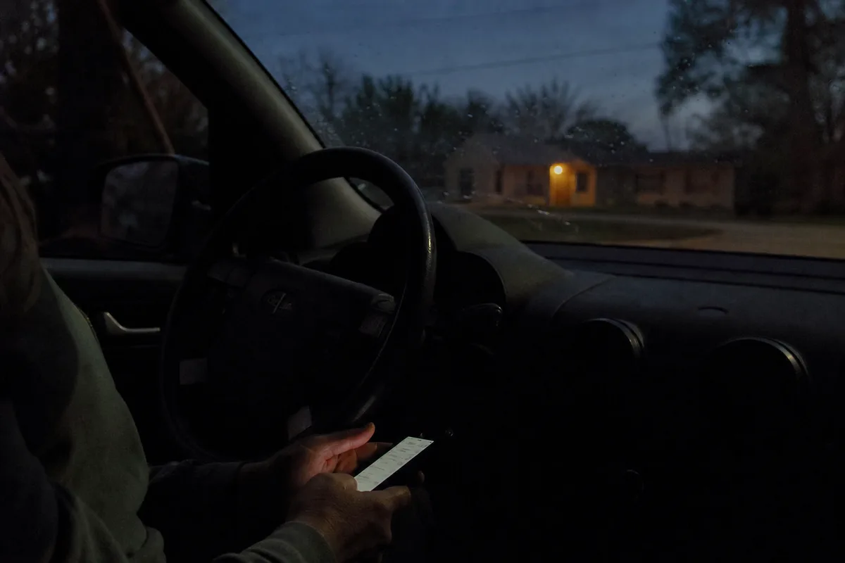 A woman's hands in her lap holding a phone, seen from the passenger seat of a parked car at dusk.
