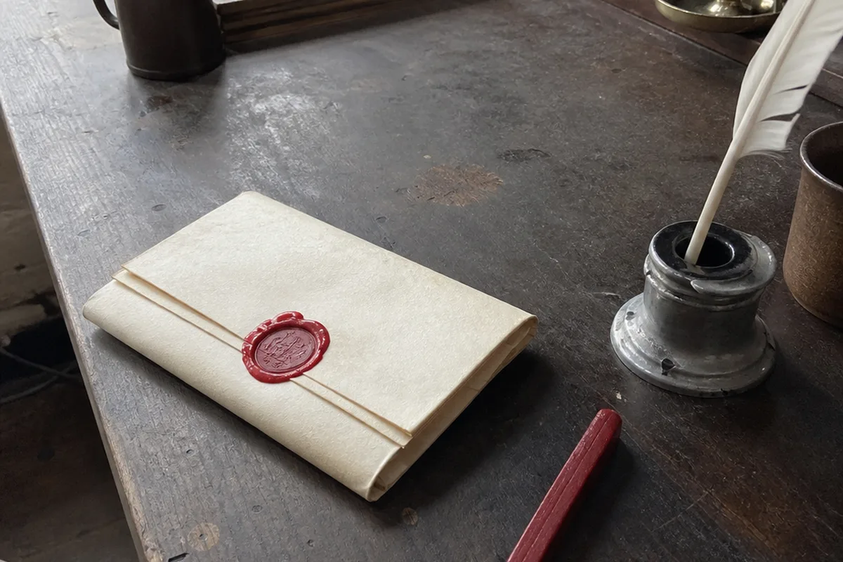 A quill pen resting on a heavy leather-bound statute book beside a pooled candle on a dark wooden desk, one warm amber light against deep green shadow.
