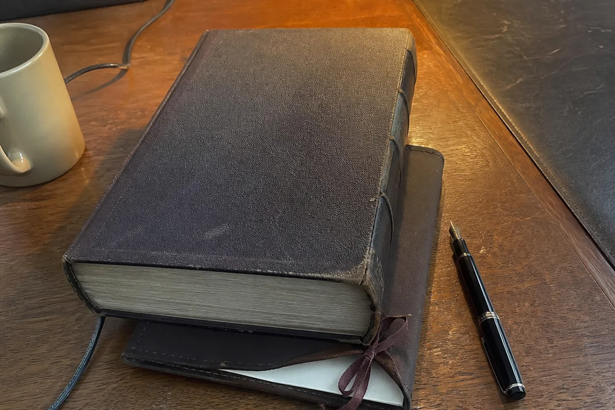 A wax-sealed envelope and a ribbon-tied will document resting on a dark wooden estate-planning desk, a magnifying glass beside them, no legible text, one warm amber light against deep green shadow.